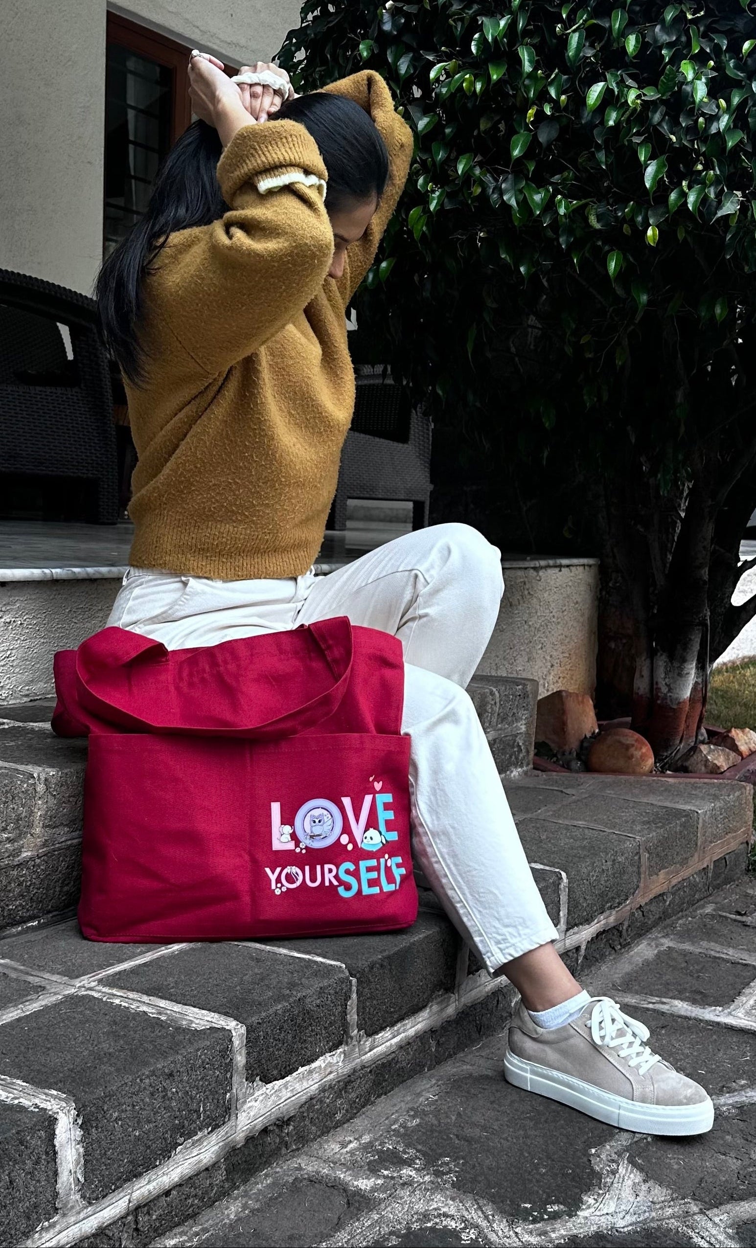 Person sitting on steps with a red bag featuring 'LOVE YOURSELF' text.